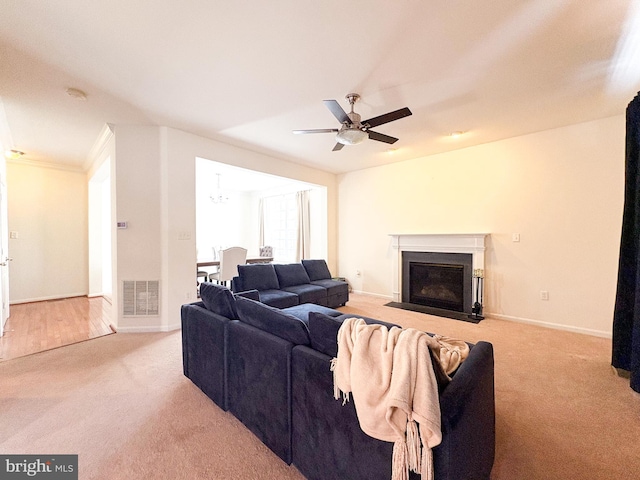 carpeted living room with ceiling fan with notable chandelier and ornamental molding