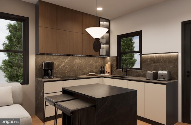 kitchen featuring hanging light fixtures, backsplash, sink, a kitchen bar, and light hardwood / wood-style floors