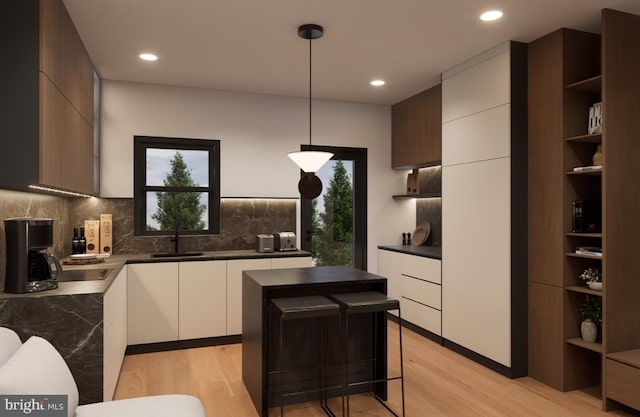 kitchen featuring sink, a kitchen island, white cabinetry, light hardwood / wood-style floors, and pendant lighting