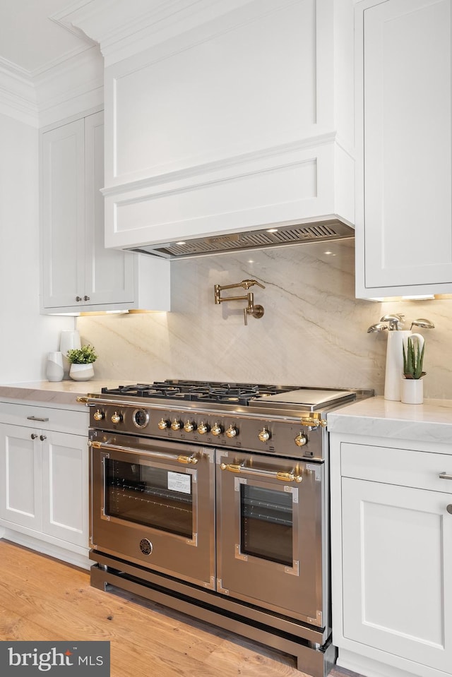 kitchen with range with two ovens, white cabinetry, light hardwood / wood-style flooring, and tasteful backsplash