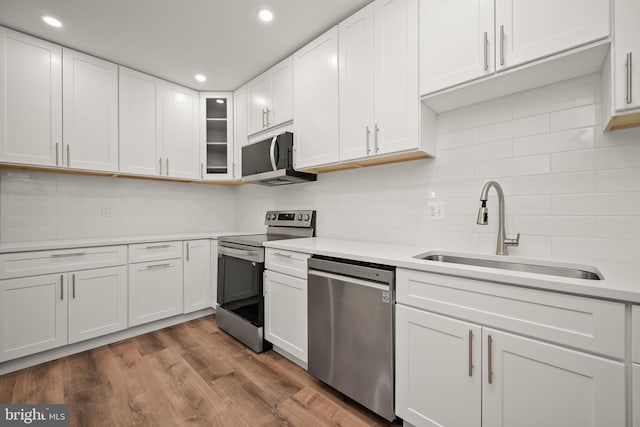 kitchen with appliances with stainless steel finishes, white cabinets, sink, and wood-type flooring