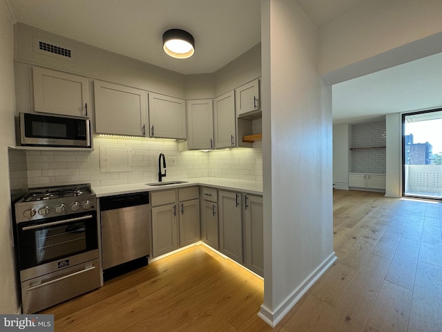 kitchen with light hardwood / wood-style floors, stainless steel appliances, tasteful backsplash, and sink