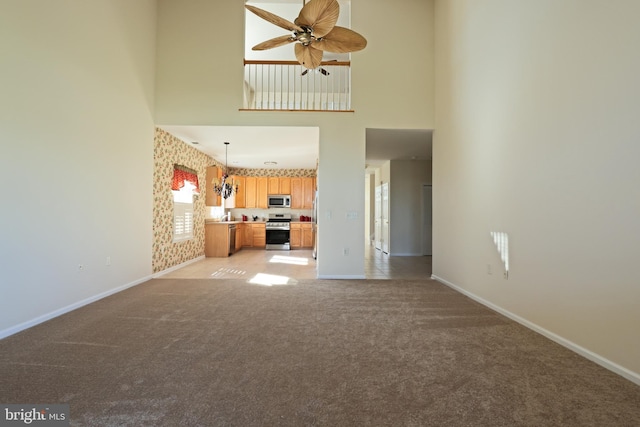 unfurnished living room with a high ceiling, light colored carpet, and ceiling fan