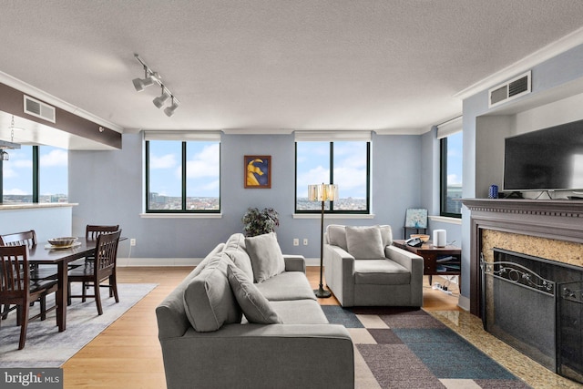 living area featuring ornamental molding, wood finished floors, a fireplace, a textured ceiling, and baseboards