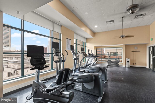 gym featuring a drop ceiling, a ceiling fan, and baseboards