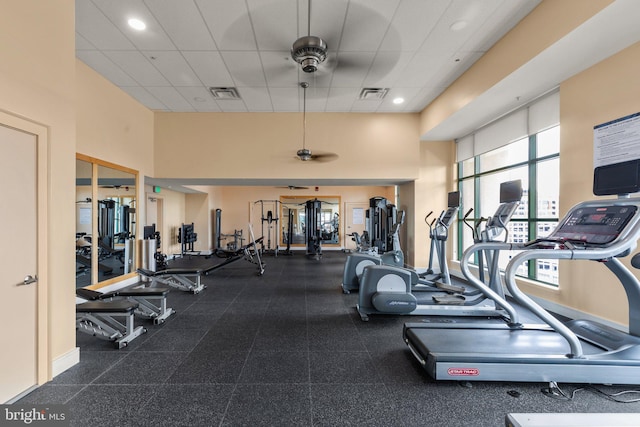 gym with a paneled ceiling, ceiling fan, and a towering ceiling