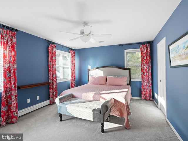 bedroom featuring a baseboard heating unit, multiple windows, light colored carpet, and ceiling fan