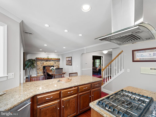 kitchen with island exhaust hood, a stone fireplace, dark hardwood / wood-style floors, ornamental molding, and light stone counters