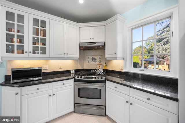 kitchen featuring decorative backsplash, stainless steel appliances, dark stone countertops, light tile patterned floors, and white cabinetry