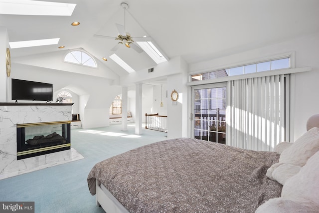 carpeted bedroom featuring ceiling fan, high vaulted ceiling, a skylight, and a fireplace