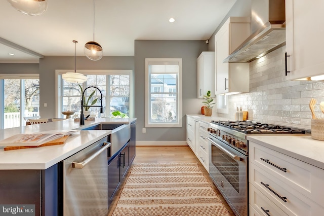 kitchen with wall chimney exhaust hood, a center island with sink, pendant lighting, stainless steel appliances, and white cabinets