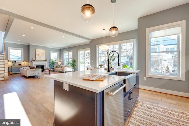 kitchen featuring decorative light fixtures, an island with sink, sink, light hardwood / wood-style floors, and plenty of natural light