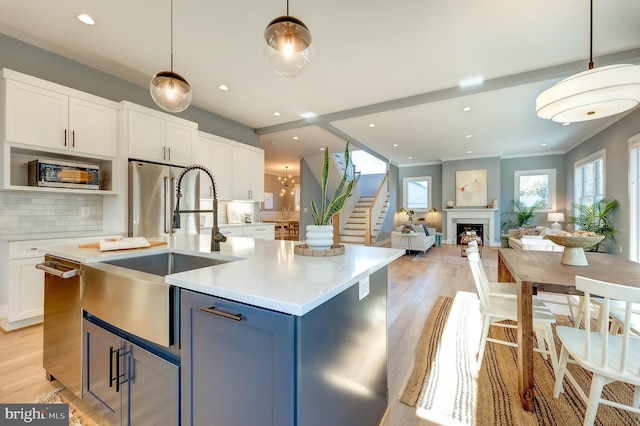 kitchen featuring a center island with sink, sink, hanging light fixtures, and white cabinets