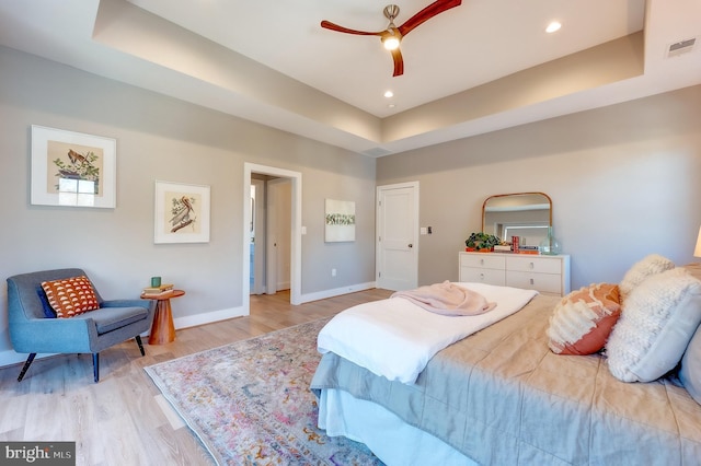 bedroom with ceiling fan, a tray ceiling, and light hardwood / wood-style flooring