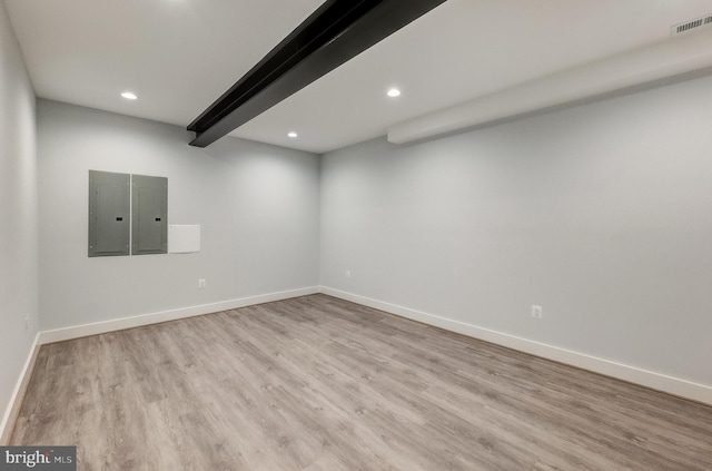 spare room with beam ceiling, electric panel, and light hardwood / wood-style flooring