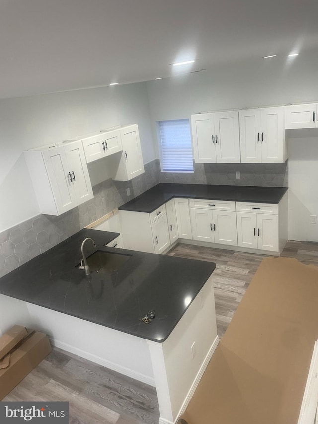 kitchen with white cabinetry, kitchen peninsula, wood-type flooring, and tasteful backsplash