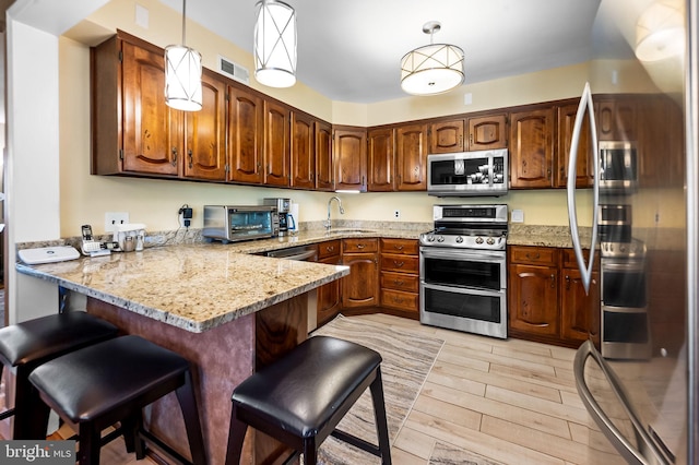 kitchen with stainless steel appliances, light wood-type flooring, pendant lighting, sink, and kitchen peninsula