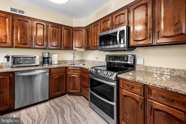 kitchen featuring stainless steel appliances, sink, light stone counters, and light hardwood / wood-style flooring