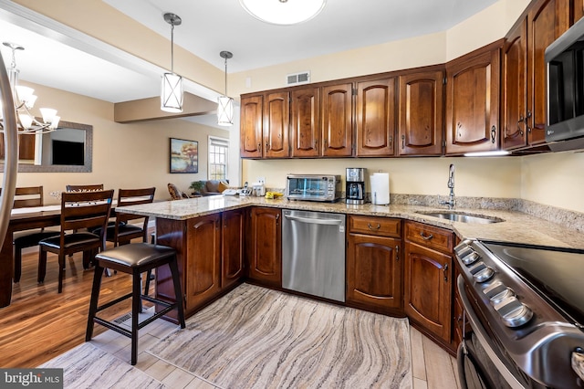 kitchen featuring stainless steel appliances, pendant lighting, light hardwood / wood-style floors, a breakfast bar, and kitchen peninsula