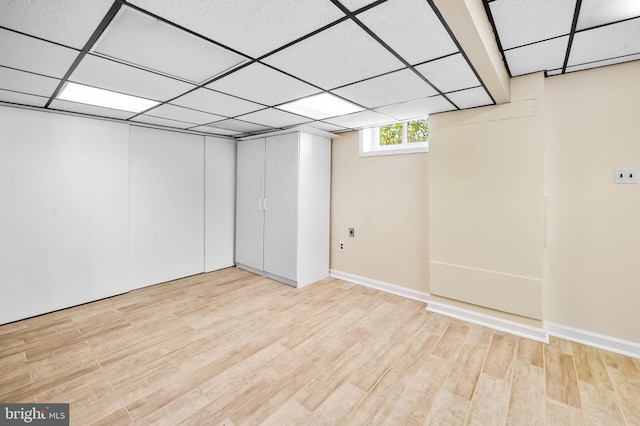 basement with light hardwood / wood-style flooring and a paneled ceiling