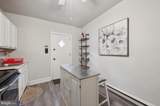 kitchen featuring a baseboard heating unit, stainless steel range, hardwood / wood-style floors, sink, and white cabinetry