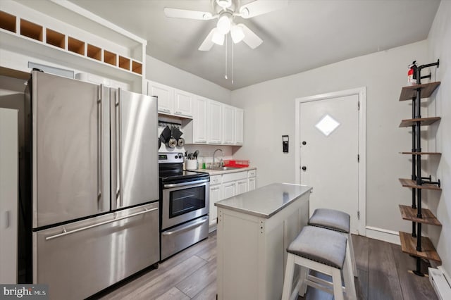 kitchen with appliances with stainless steel finishes, a kitchen bar, a kitchen island, white cabinets, and light hardwood / wood-style flooring