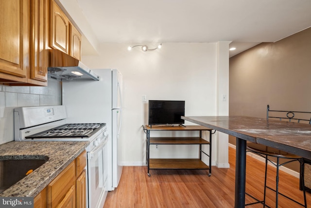 kitchen with tasteful backsplash, light stone countertops, light wood-type flooring, white gas range, and range hood