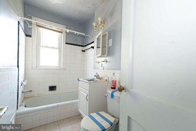 full bathroom with tile patterned floors, toilet, tiled shower / bath, tile walls, and vanity