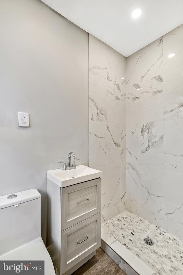 bathroom with vanity, a tile shower, hardwood / wood-style flooring, and toilet