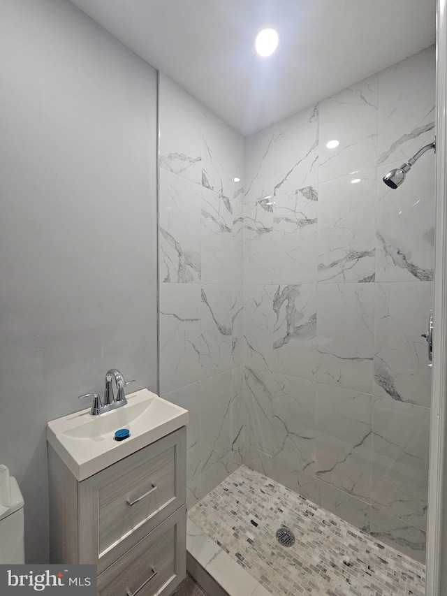 bathroom featuring vanity, a tile shower, and toilet