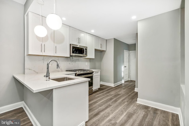 kitchen featuring wood-type flooring, sink, pendant lighting, white cabinetry, and appliances with stainless steel finishes