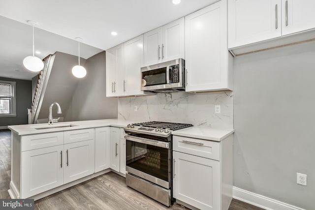 kitchen with hanging light fixtures, sink, white cabinets, appliances with stainless steel finishes, and light hardwood / wood-style floors