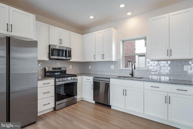 kitchen featuring white cabinets, sink, decorative backsplash, light wood-type flooring, and appliances with stainless steel finishes