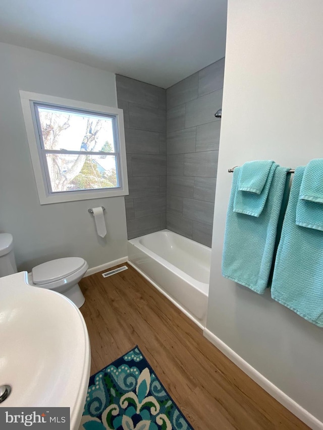 bathroom featuring toilet, tiled shower / bath, and wood-type flooring