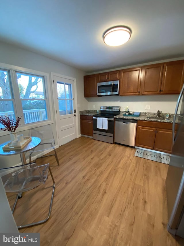 kitchen featuring sink, light wood-type flooring, dark stone counters, and appliances with stainless steel finishes