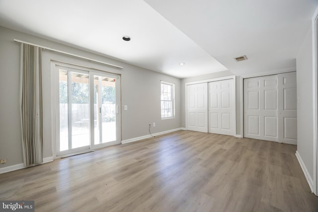 unfurnished bedroom featuring light hardwood / wood-style flooring, access to exterior, and multiple closets