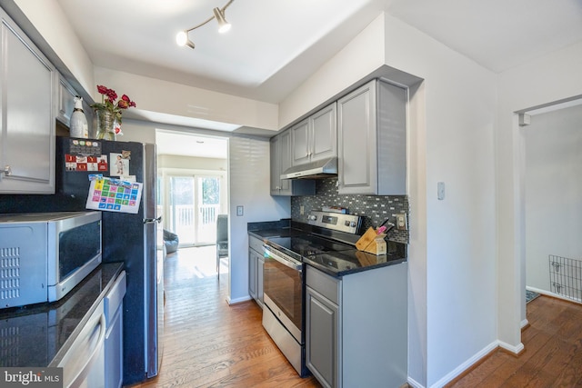 kitchen featuring gray cabinetry, stainless steel appliances, wood-type flooring, and decorative backsplash