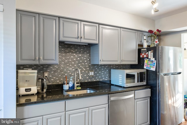 kitchen featuring backsplash, appliances with stainless steel finishes, dark stone counters, gray cabinetry, and sink