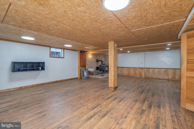 basement featuring dark hardwood / wood-style flooring, a wood stove, and wood walls