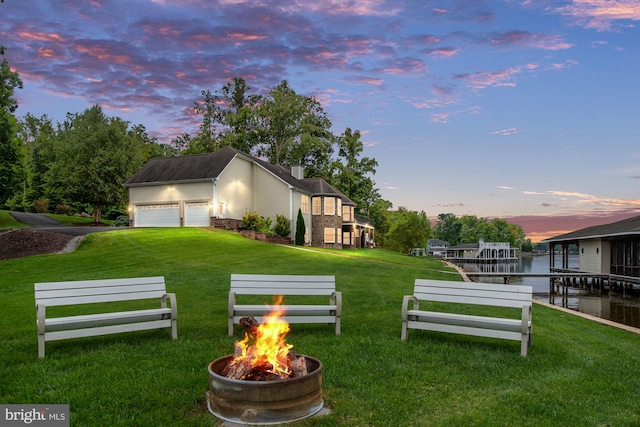 yard at dusk featuring a garage, a water view, an outdoor structure, and an outdoor fire pit