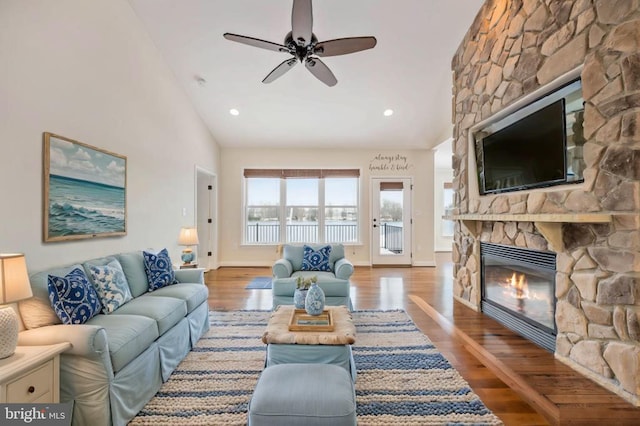 living room featuring a stone fireplace, ceiling fan, hardwood / wood-style floors, and high vaulted ceiling