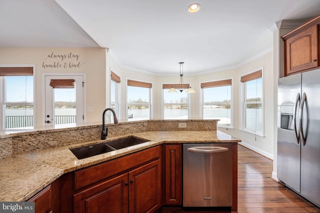 kitchen with light stone countertops, sink, stainless steel appliances, decorative light fixtures, and a water view