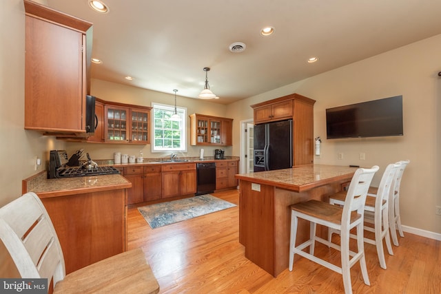 kitchen featuring kitchen peninsula, a breakfast bar area, light wood-type flooring, black appliances, and pendant lighting