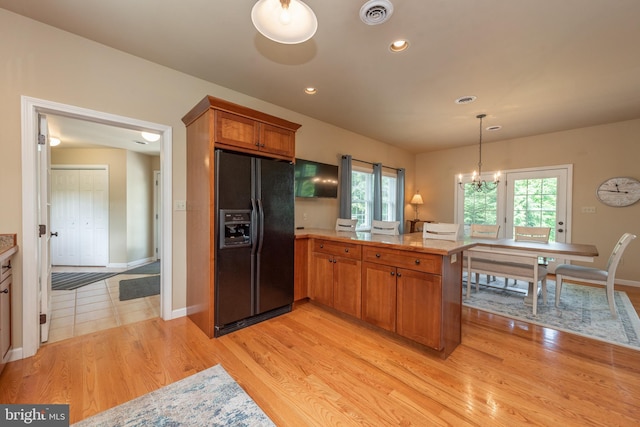 kitchen featuring black refrigerator with ice dispenser, kitchen peninsula, a chandelier, pendant lighting, and light hardwood / wood-style floors