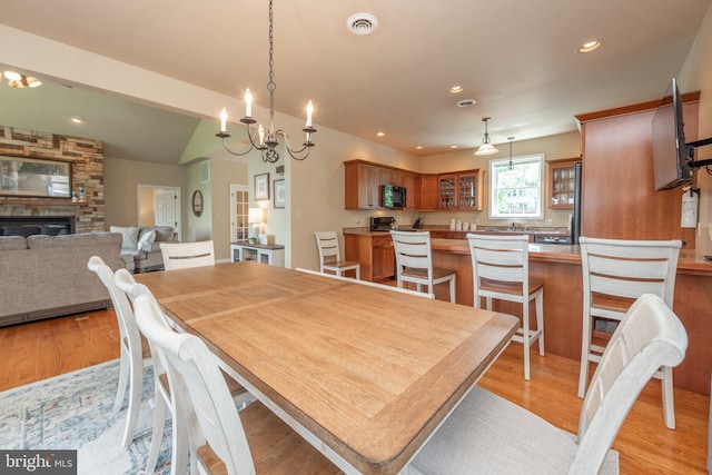 dining room with light hardwood / wood-style floors, a notable chandelier, lofted ceiling, and a fireplace