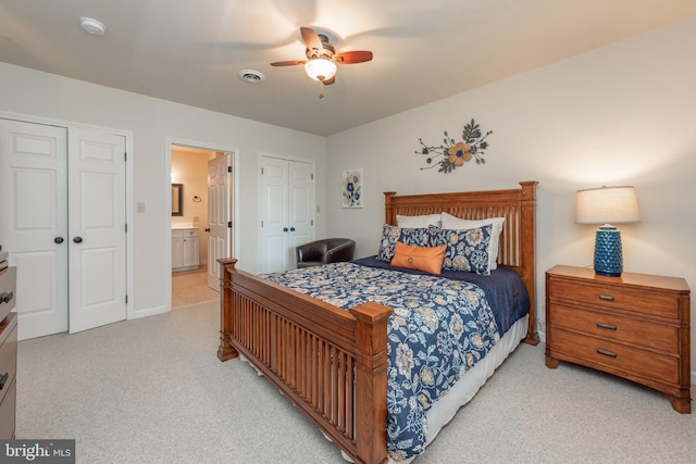 bedroom with connected bathroom, light carpet, multiple closets, and ceiling fan