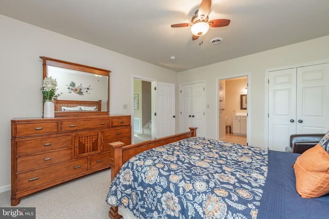 bedroom with connected bathroom, ceiling fan, two closets, and light colored carpet