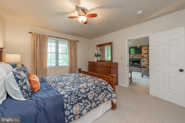 carpeted bedroom featuring a stone fireplace and ceiling fan