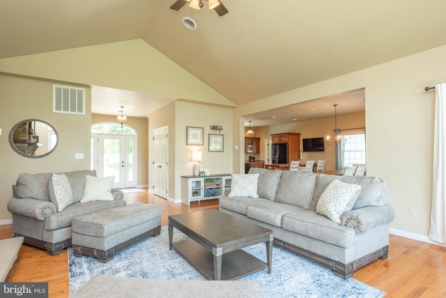 living room with a wealth of natural light, high vaulted ceiling, ceiling fan with notable chandelier, and light hardwood / wood-style floors