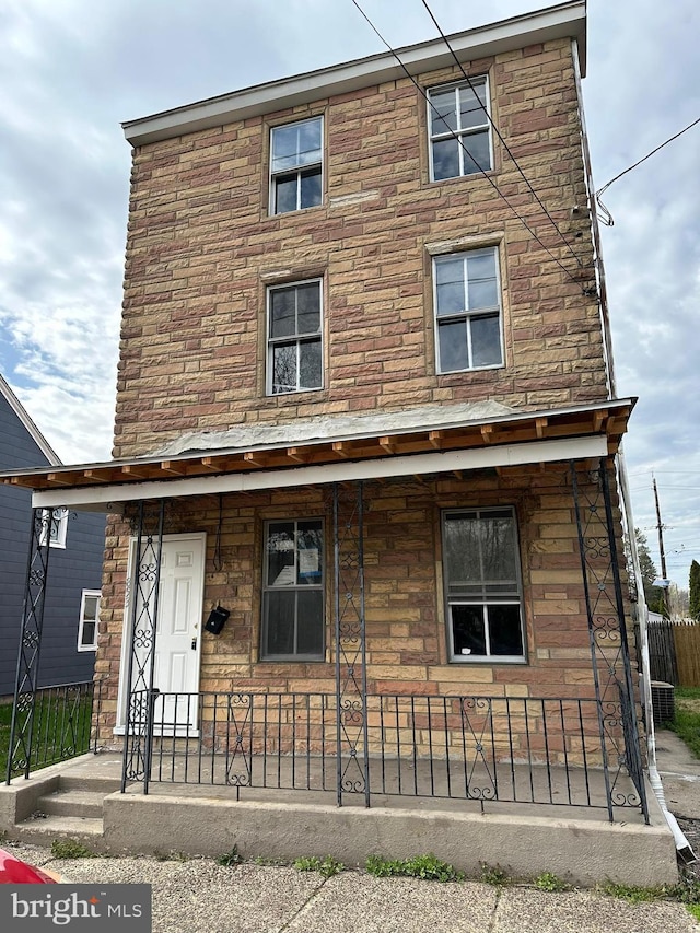 view of front of house featuring stone siding, covered porch, and fence